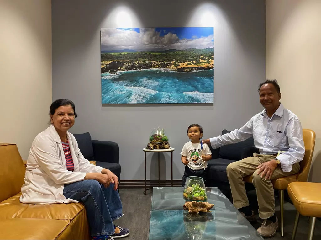 In the image, there are three individuals seated together on a couch in an office environment. They appear to be engaged in a conversation or meeting.