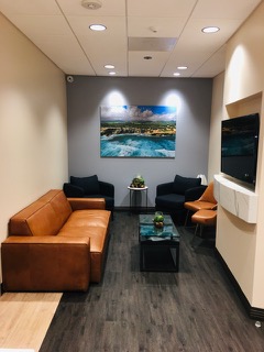 The image displays a modern waiting room with a clean and minimalist design, featuring a couch, chairs, a television, and a large picture on the wall.
