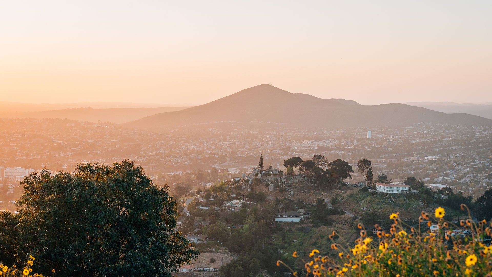 The image depicts a scenic view of a cityscape at sunset with a prominent hill in the background, bathed in warm light.
