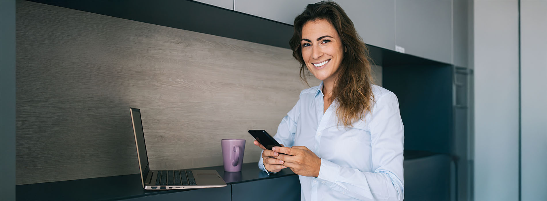 A woman in a professional setting, holding a phone, smiling, with a blurred background.