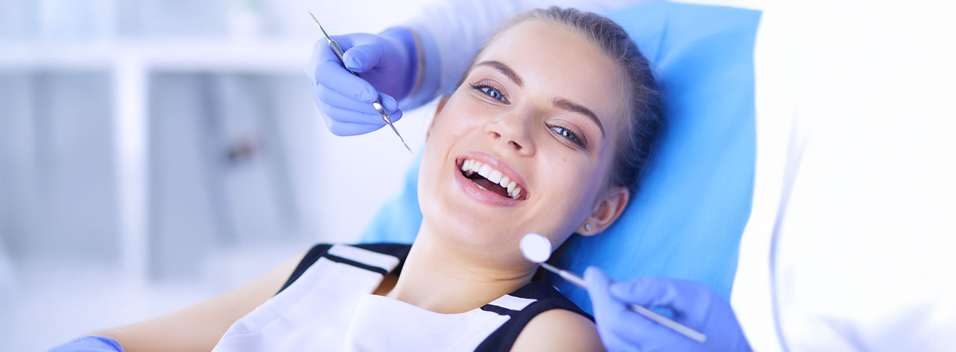 The image shows a woman sitting in a dental chair with her eyes closed, smiling slightly, while receiving dental treatment under the care of a dentist wearing gloves and a face mask.