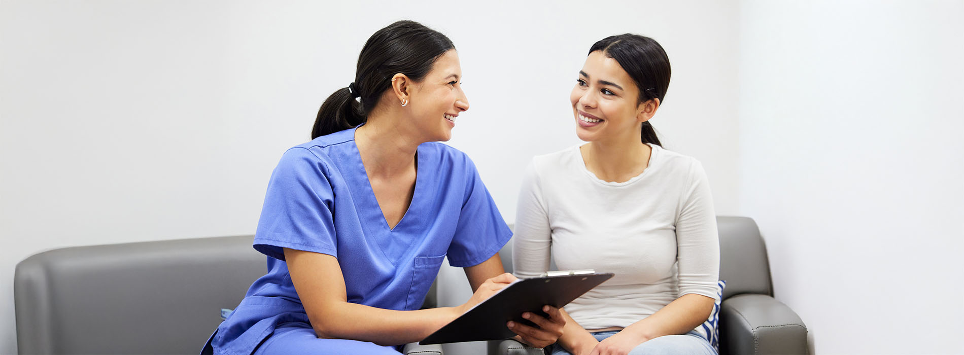 A photograph of two women in a professional setting, one holding a tablet with both smiling at the camera, with an overlaid watermark or logo.