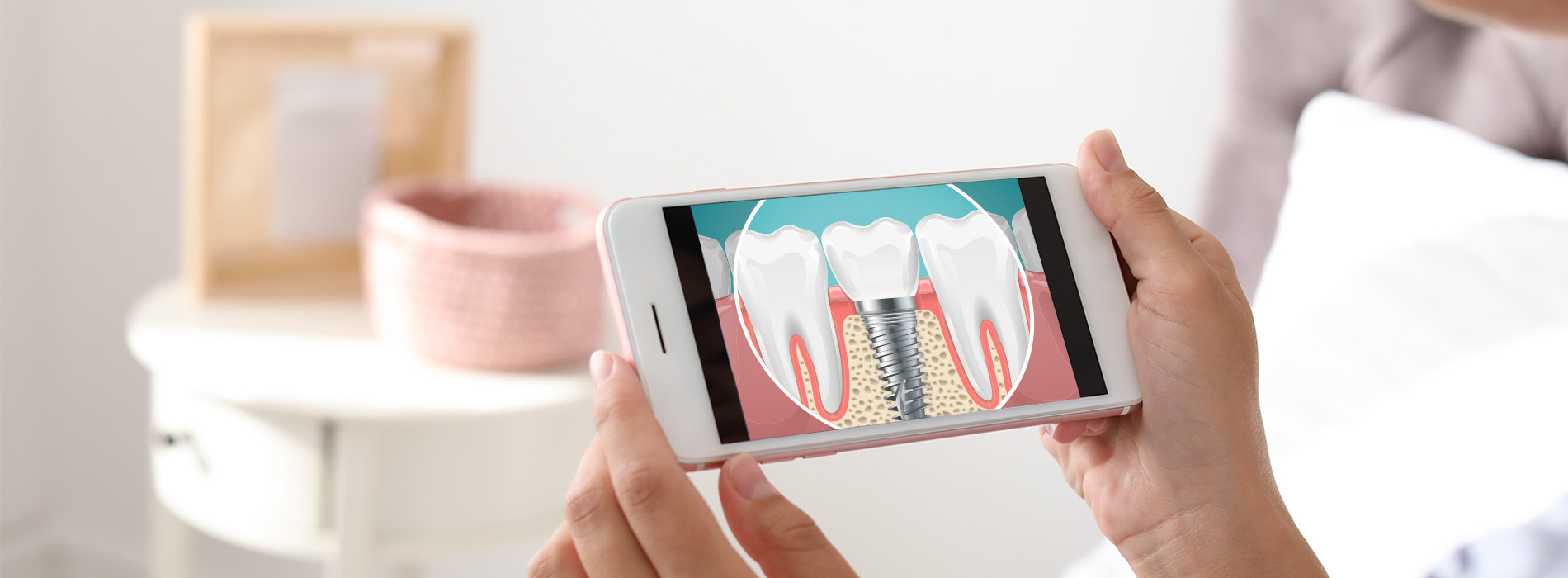 A person holding a smartphone displaying an illustration of a toothbrush with bristles and a toothpaste tube, set against a blurred background that includes a table and a pink object.