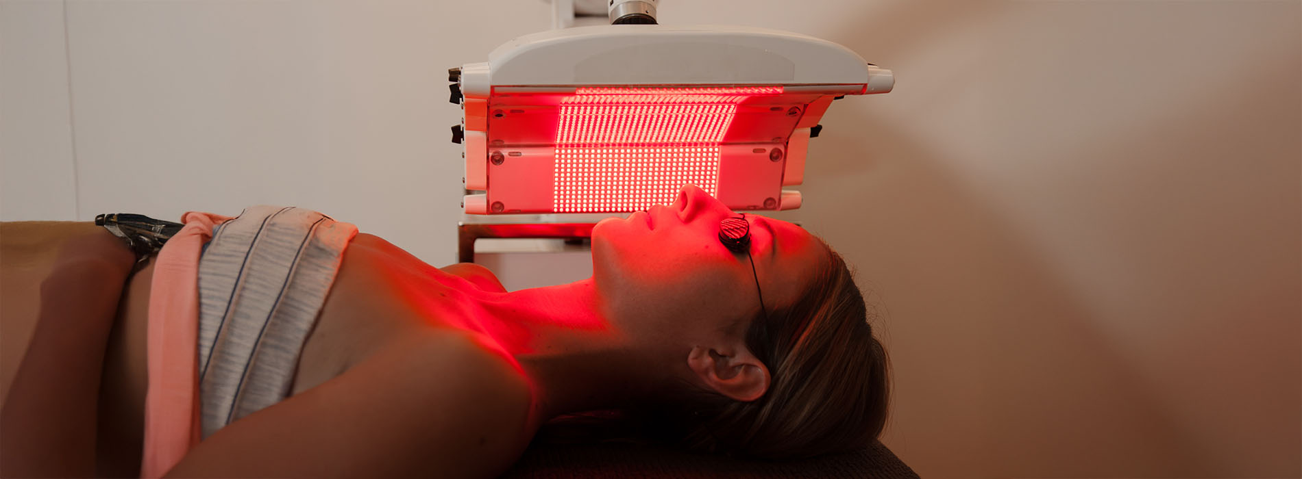 A person lying down with their head on an infrared light device, which appears to be a facial treatment machine.