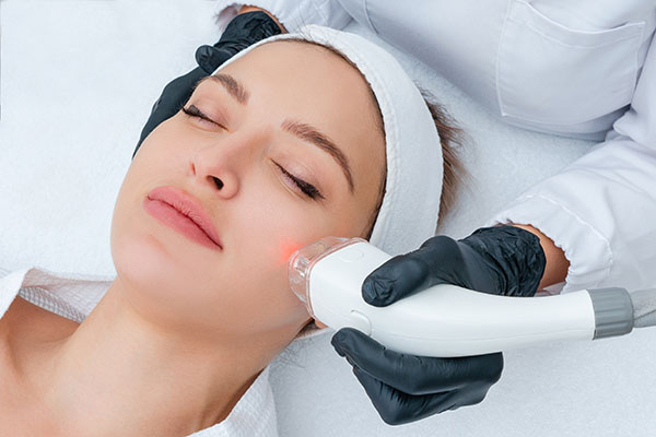 A person receiving a facial treatment with a device held by another individual, both in a clinical setting.