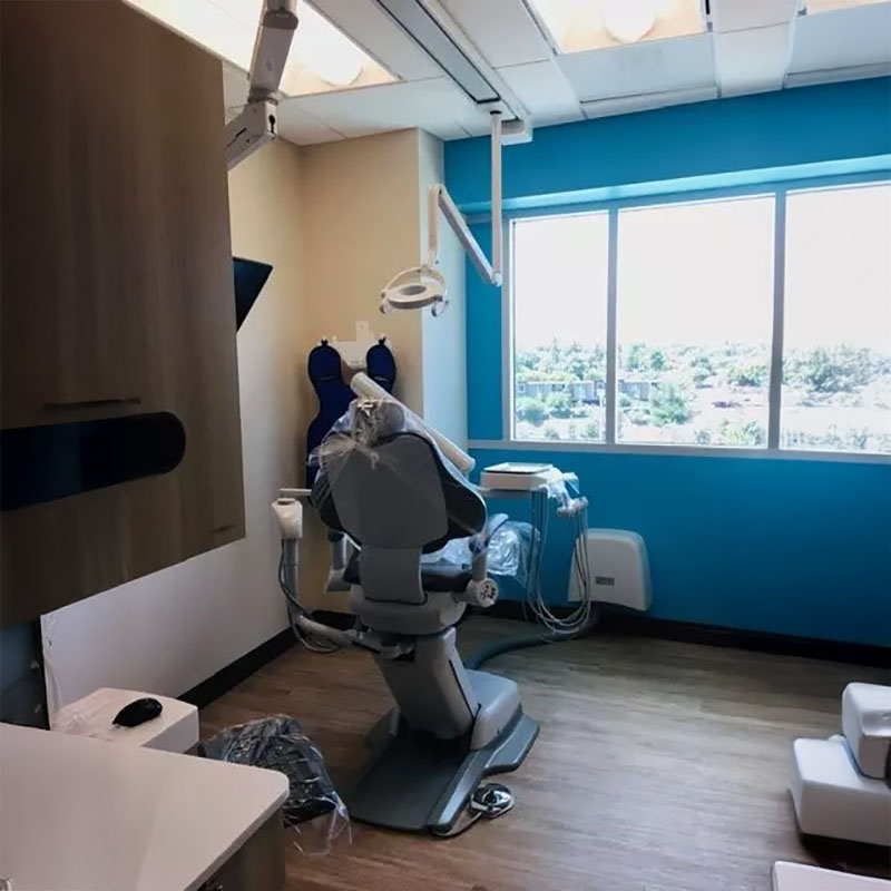 The image shows a modern dental office interior with a dental chair, dental equipment, and a window view.