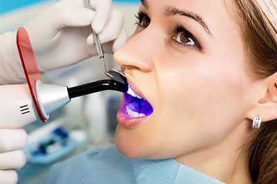 Woman receiving dental treatment with purple light device.