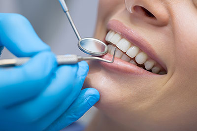 The image shows a person receiving dental care with a dental hygienist performing a teeth cleaning procedure using a mirror, dental instruments, and a water spray.