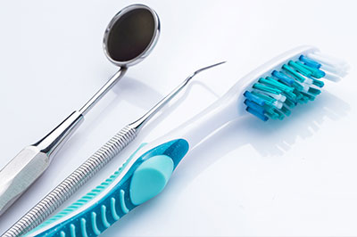 The image shows dental tools including a toothbrush with blue bristles, a pair of tweezers, and a dental mirror on a white background.