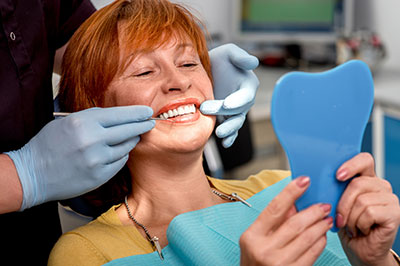 A woman sits in a dental chair, receiving oral care, with a dental professional attending to her.