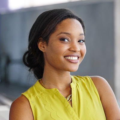 A woman with a radiant smile poses confidently against a backdrop of a modern building.