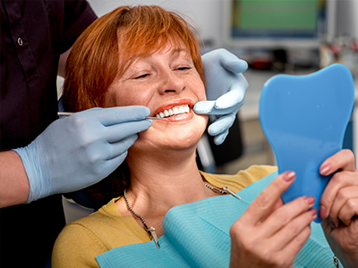 A woman receiving dental care, seated in a dental chair with a hygienist holding tools and a blue mouthguard, wearing gloves and a mask, in an office setting.