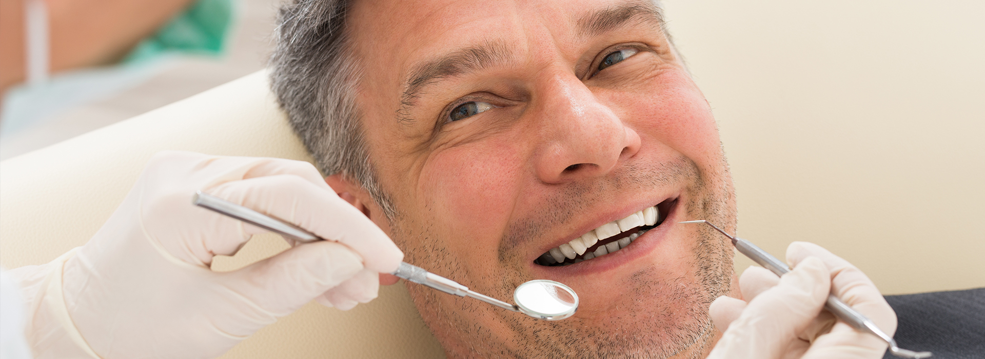 A man in a dental chair receiving a teeth cleaning from a dentist, with a toothbrush and dental tools visible.