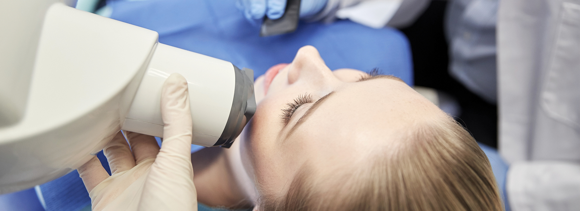 A woman receiving dental care with a dentist using a microscope to examine her teeth.