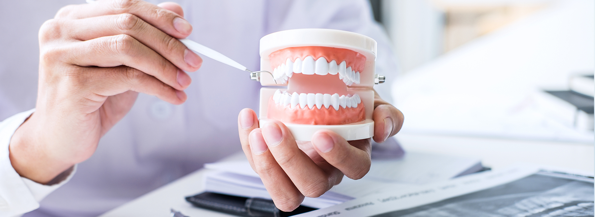 A person s hand holding a toothbrush with toothpaste in front of a blurred background featuring a dental office setting.