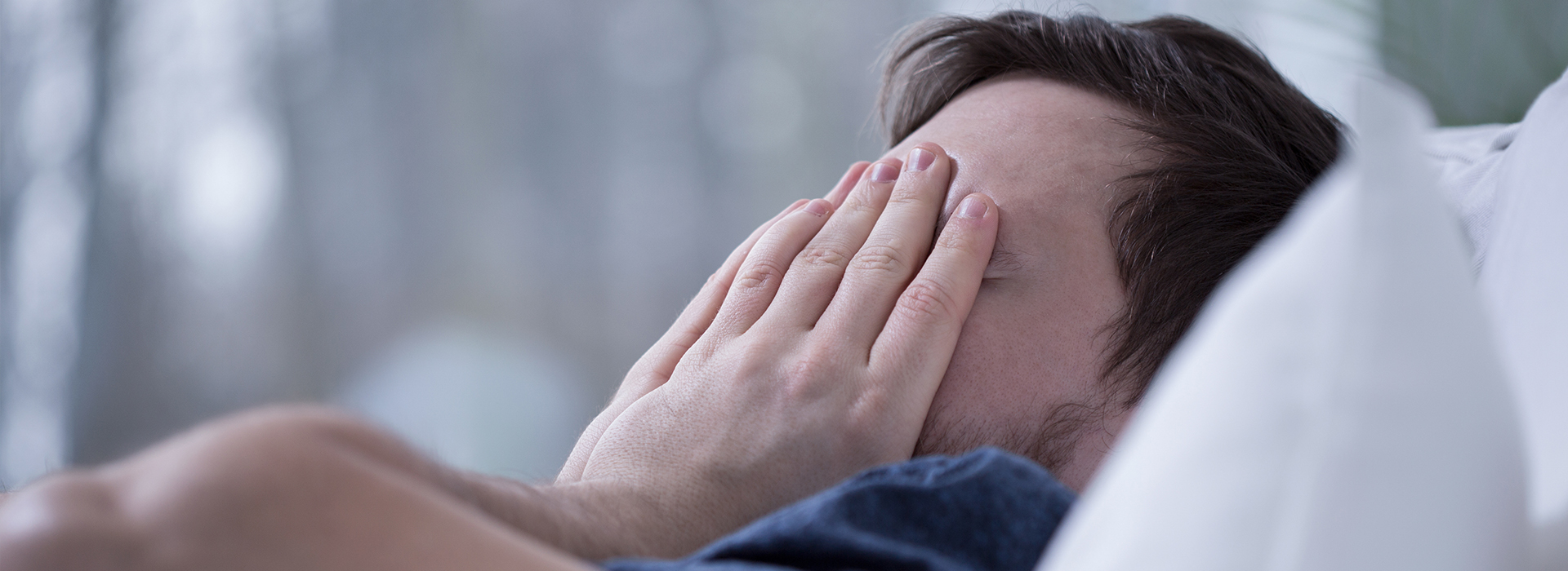 The image shows a person lying down with their face covered by their hands, appearing to be in a state of distress or discomfort.