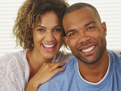 A man and woman smiling together, with the man wearing a short beard and the woman with curly hair, both dressed casually.