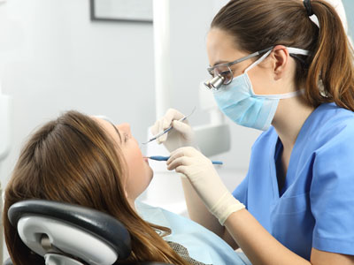 A dental hygienist is performing a cleaning procedure on a patient s teeth while wearing protective eyewear, gloves, and a mask.