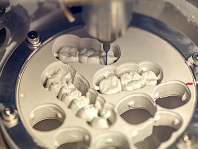 The image shows a close-up view of a dental implant fixture with multiple teeth-like structures and a drill, indicating a dental manufacturing process.