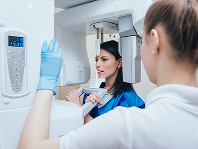 A woman in blue scrubs stands next to a large white 3D scanner, with another person observing the process.