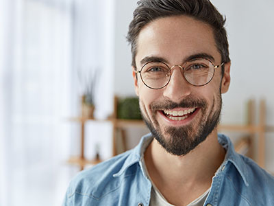 A bearded man with glasses, smiling at the camera, against a blurred background that suggests an indoor setting.