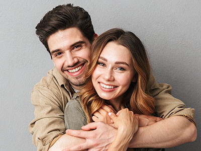 A man and woman hugging each other, smiling and appearing happy against a neutral background.