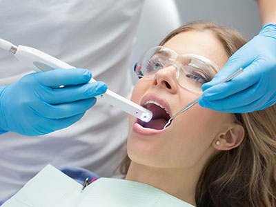 A dental professional using a device to examine a patient s teeth during an appointment.