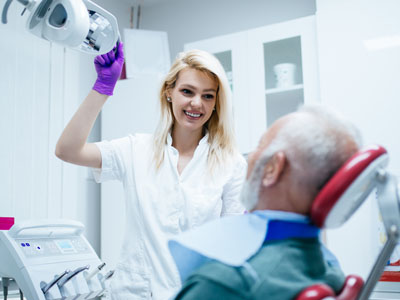 A female dental professional assisting an elderly man with a medical device during a dental procedure.