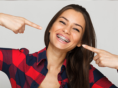 The image shows a woman with a bright smile pointing towards her teeth, wearing a flannel shirt with a playful pose.