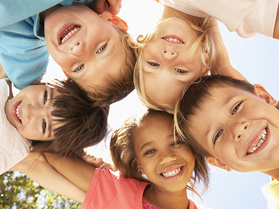 The image shows a group of children standing in a circle, smiling at the camera.