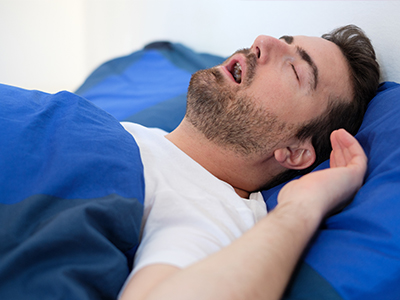 A man lying in bed with his eyes closed, appearing to be asleep or resting.