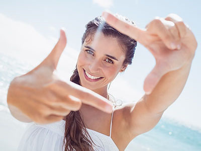 A woman with blonde hair smiles at the camera while holding up her hand to frame the shot.