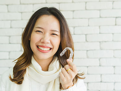 Woman holding a clear plastic dental retainer with a smile on her face.